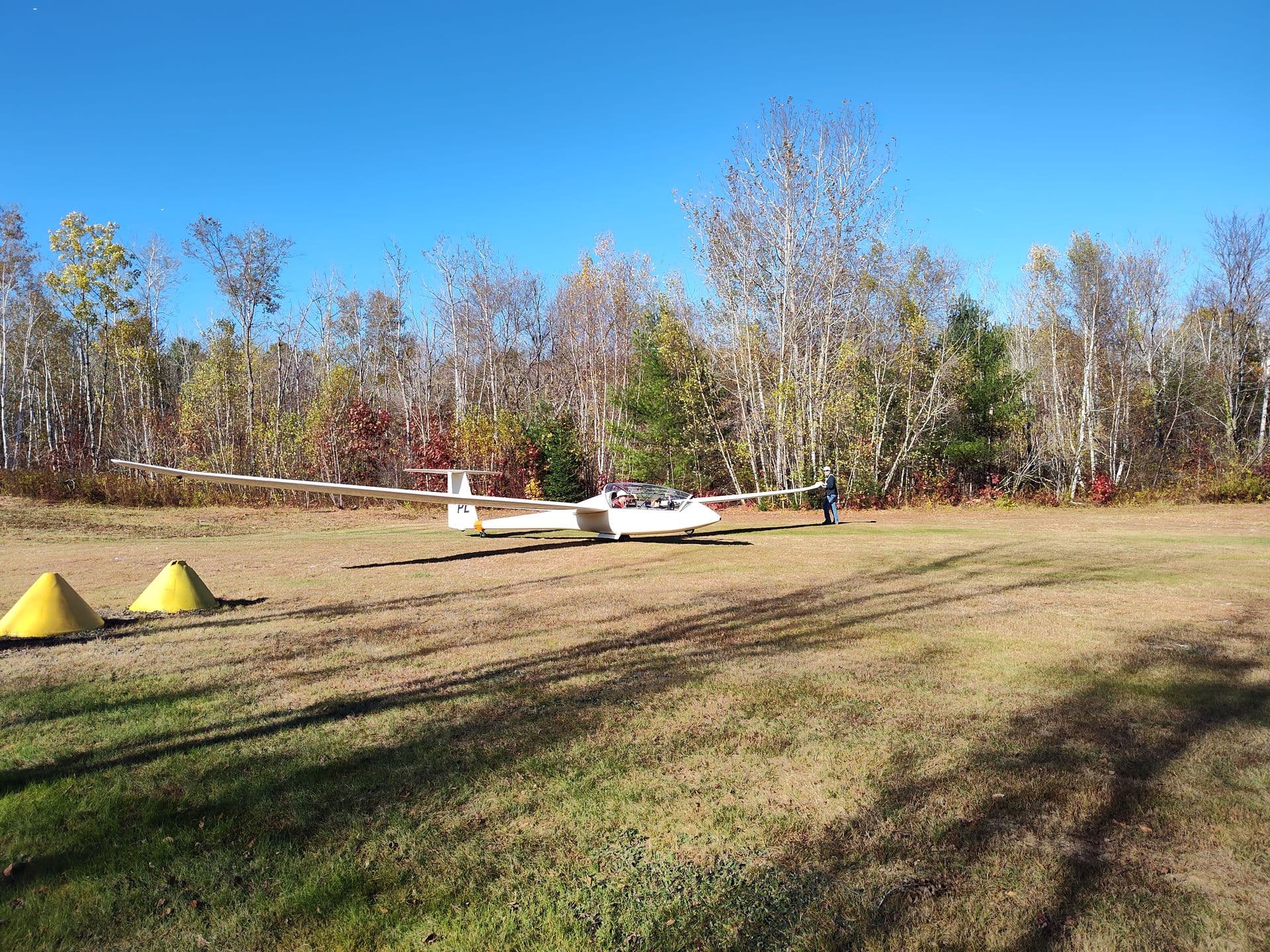 A white glider on the grass between yellow runway cones at Gorham