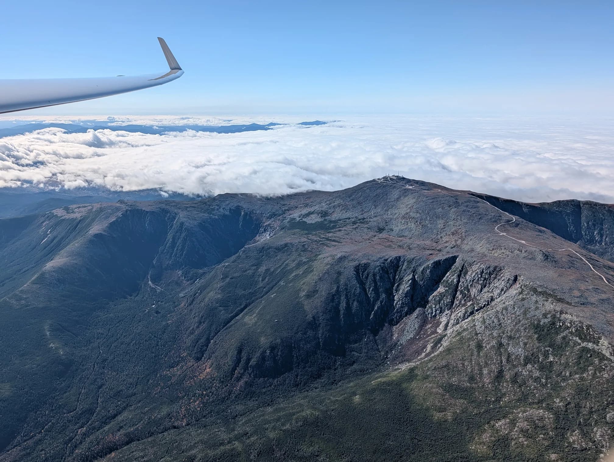 Mount Washington's summit and the Auto Road seen from the wing, a wall of cloud beyond